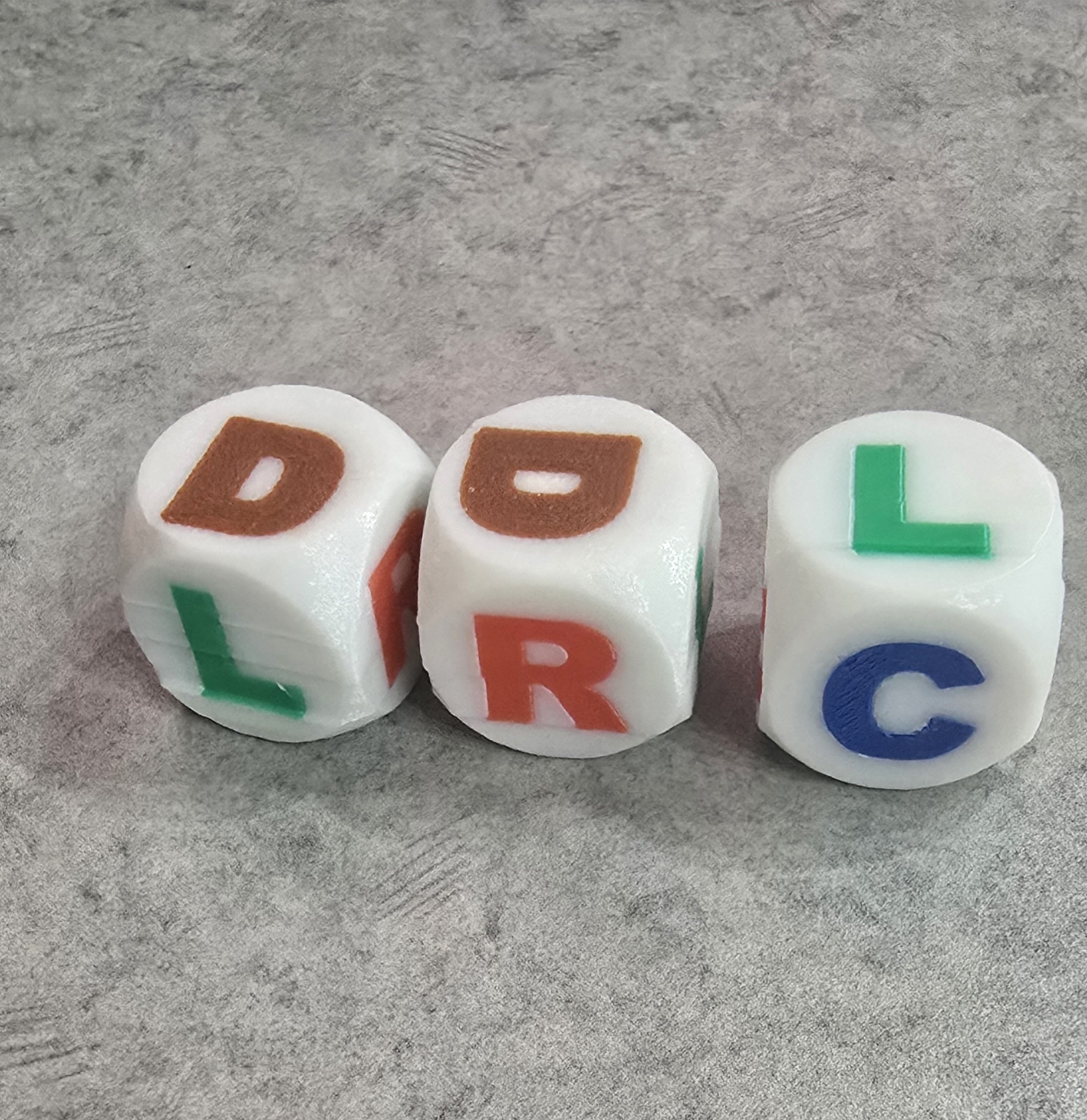Three white dice with contrasting colored letters.